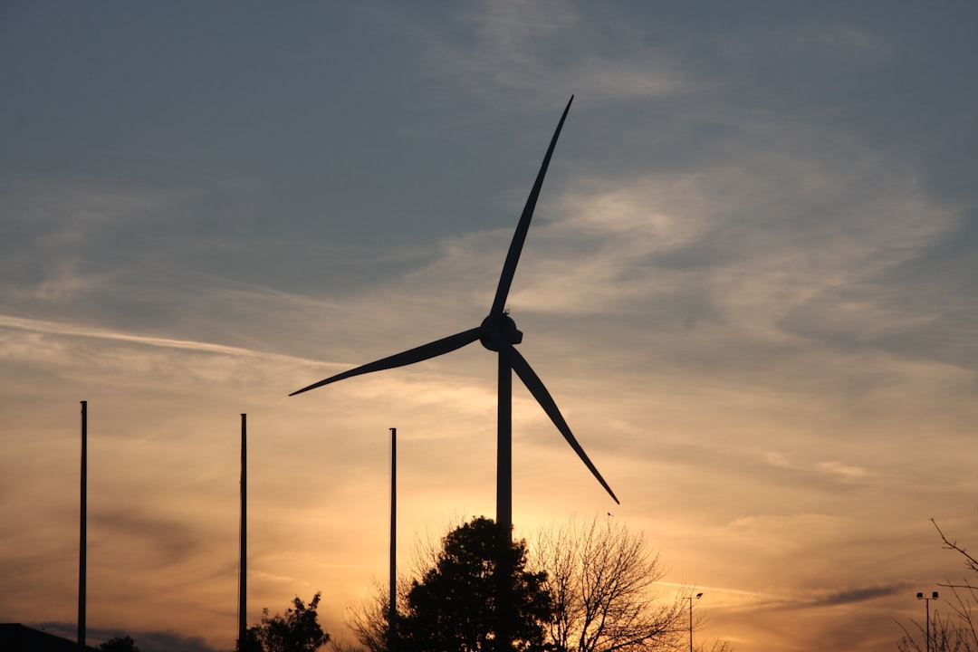 Éolienne sous un ciel bleu et orangé, dans une zone industrielle.